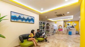 Un espace d’accueil au design moderne, comprenant un comptoir de réception, un coin salon avec des fauteuils verts et un grand tableau abstrait accroché au mur.