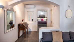 Habitación de hotel con cama, sofá, escritorio con espejo y un pasillo que conduce a otra habitación.