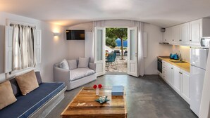 Un interior moderno con un sofá, una mesa de centro de madera, una cocina con armarios blancos y vistas al exterior.