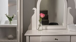 Un tocador blanco con un espejo grande, un florero con una rosa rosa y una cesta decorativa.