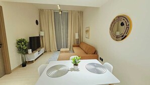 A modern living room with a sofa, a TV, a dining table with placemats, and a potted plant. - OYO HOME 1404 Premium 1bed Apt At Jvc Be (Dubai)