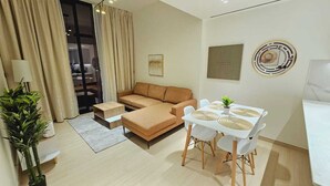 A modern living room with a sofa, a dining table with chairs, and a potted plant. - OYO HOME 1404 Premium 1bed Apt At Jvc Be (Dubai)