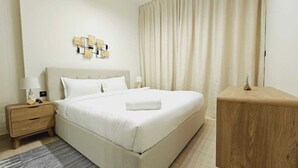 A neatly arranged hotel room with a large bed, a bedside table with a lamp, a small wooden nightstand, and a wooden side table. - OYO HOME 1404 Premium 1bed Apt At Jvc Be (Dubai)
