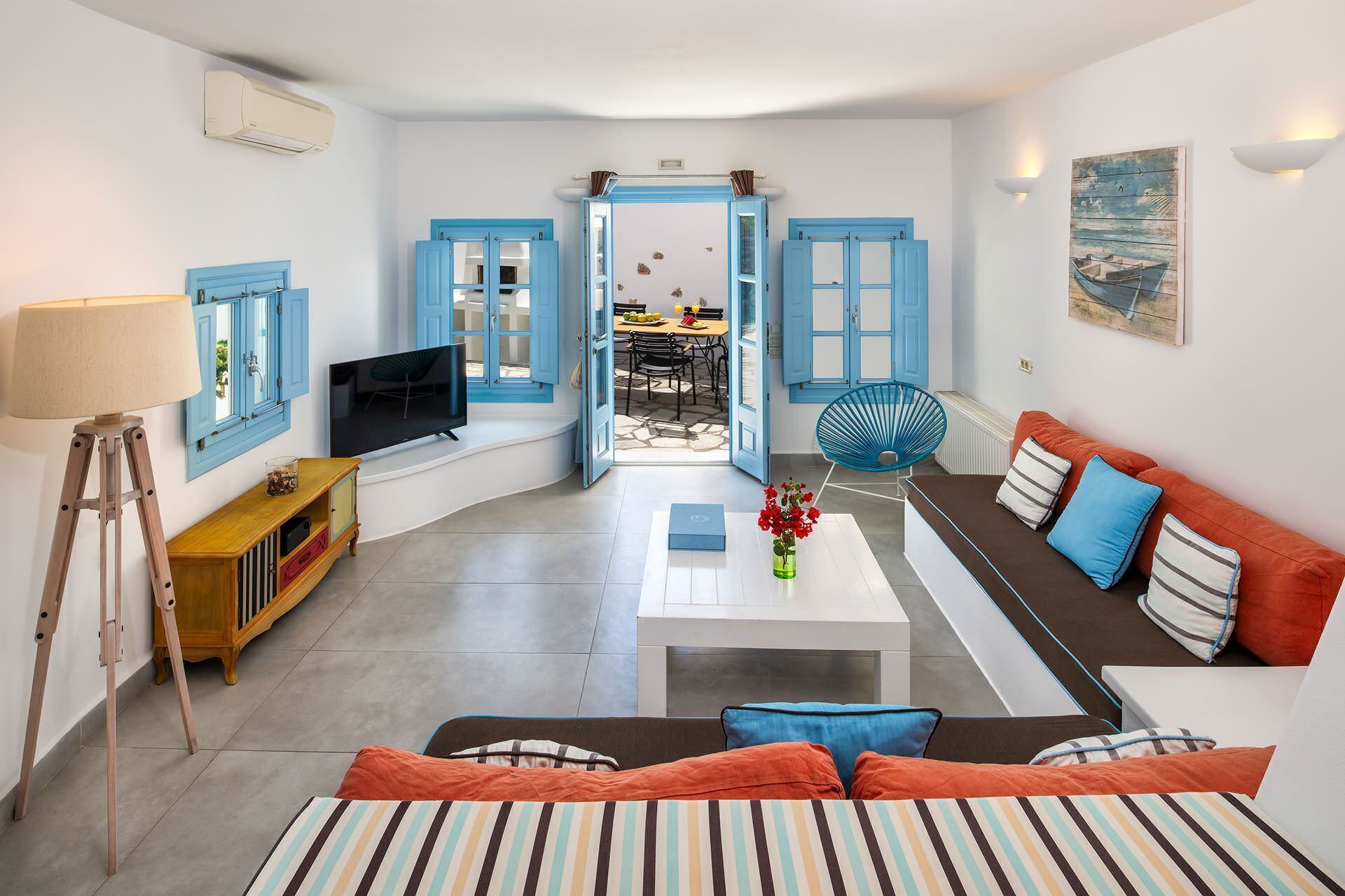 Una sala de estar moderna con un sofá, una mesa de centro y un televisor. Se ve un comedor a través de una puerta abierta.