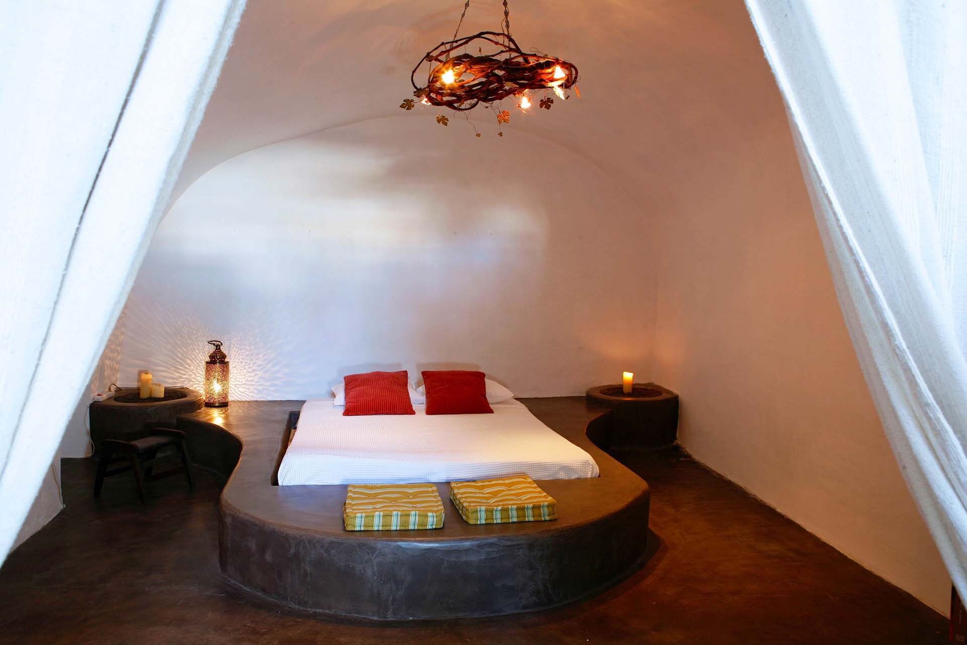 A cozy, tent-like bedroom with a bed centered on a circular platform, two bedside tables with candles, and a hanging light fixture.