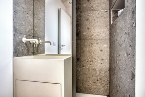 A modern bathroom with a white sink, a vertical mirror, and a shower area with a glass door. - Modern Flat Near Historic Castle (Milan)