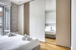 A modern bedroom with a large bed, a brick accent wall, and a sliding door leading to a balcony. - Modern Flat Near Historic Castle (Milan)