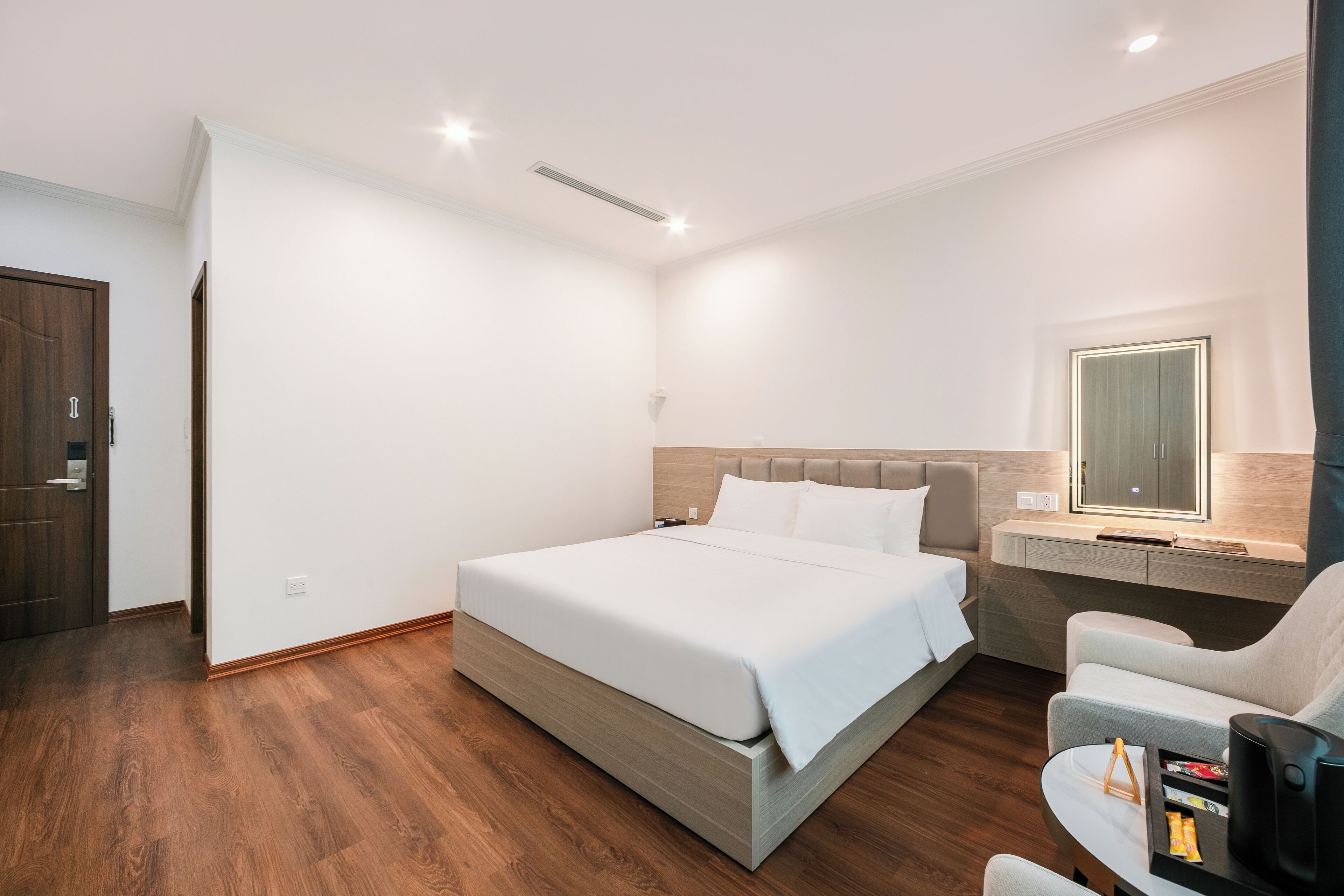 A modern hotel room with a large bed, a desk with a chair, and a small seating area.
