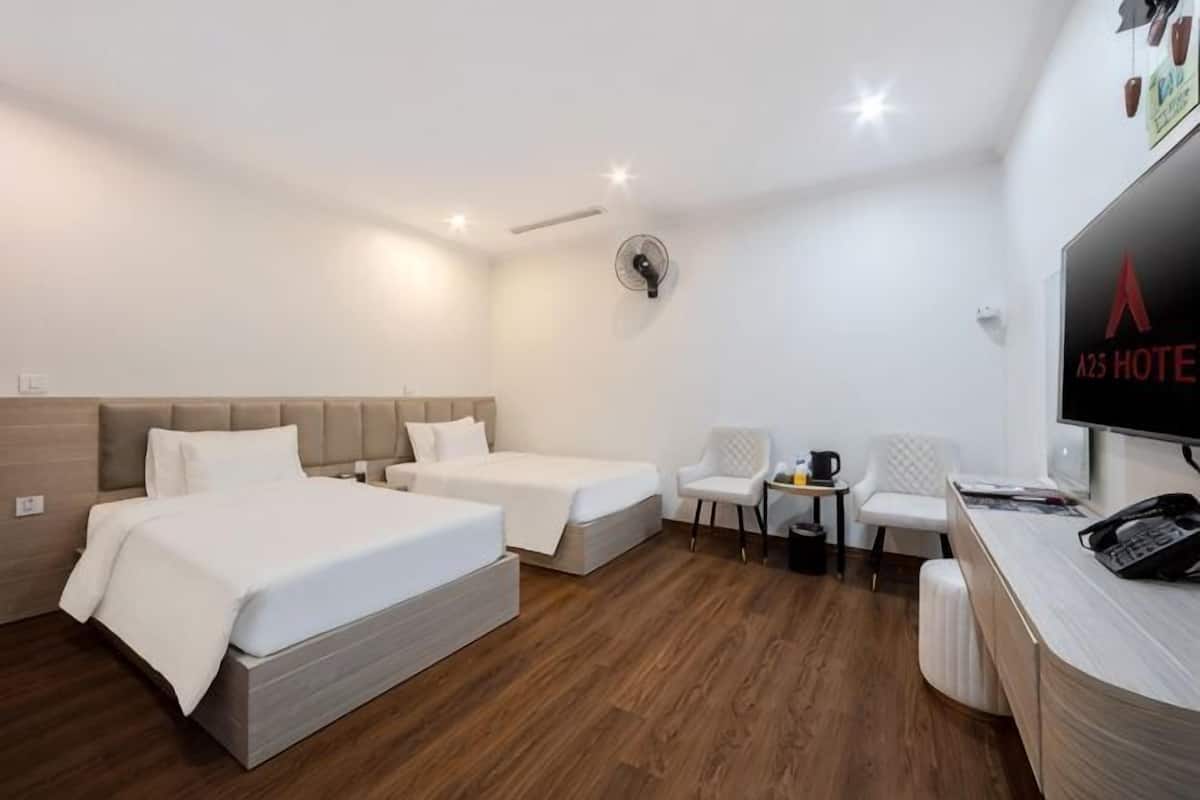 Una habitación de hotel con dos camas, un escritorio, una silla, un televisor y un ventilador.