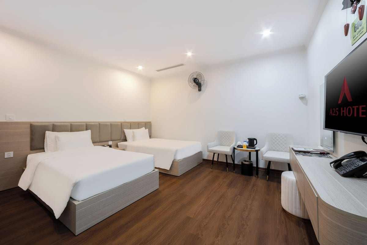 Habitación de hotel con dos camas, un escritorio, una silla, una mesita con una cafetera y un televisor.