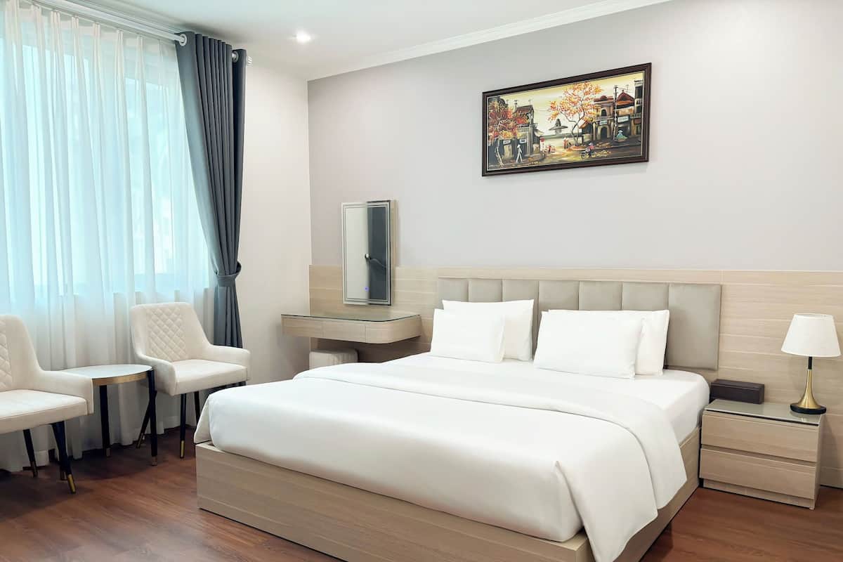 Una habitación de hotel con una cama grande, una mesita de noche, una silla, un escritorio, una lámpara y un cuadro en la pared.