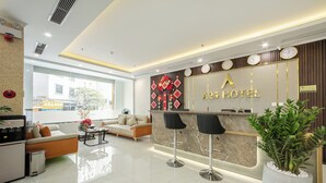 A hotel reception area with a marble counter, two black bar stools, a sofa, and a potted plant. - A25 Hotel - Hoang Dao Thuy 2 (Hanoi)