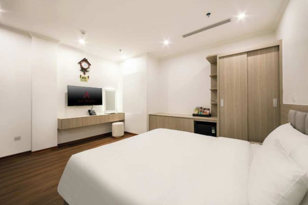 Een moderne hotelkamer met een groot bed, een flatscreen televisie aan de muur, een houten garderobe en een klein nachtkastje met een lamp.