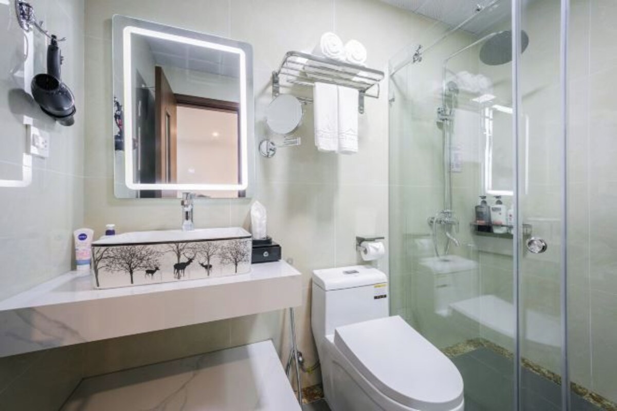 Een moderne badkamer met een glazen douchecabine, een witte wastafel met spiegel en een toilet.
