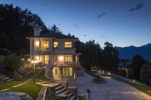 Une maison à plusieurs étages, dotée d’une façade en pierre, d’un espace extérieur couvert et offrant une vue sur les montagnes en arrière-plan.