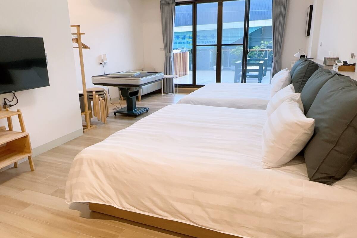 A hotel room with two beds, a TV, a desk, and a view of the outside.