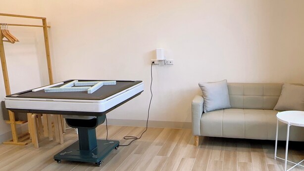 A room with a massage table, a sofa, a small table, and a window with curtains. - Hidden Villa (Chaozhou)