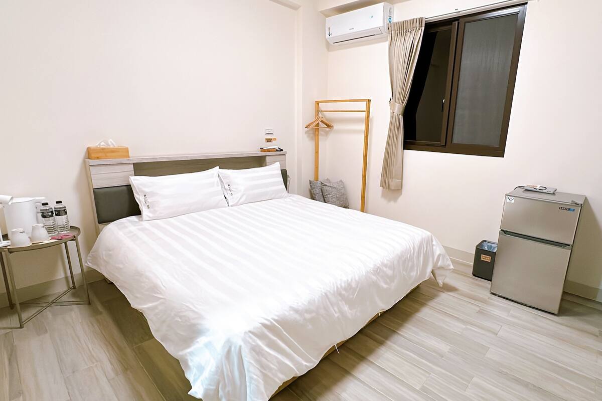 A hotel room with a bed, bedside table, and a small refrigerator.