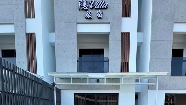 Un espace extérieur moderne aménagé avec des canapés et des tables, une terrasse en bois et un bâtiment sur lequel on peut lire l’inscription « Villa ».