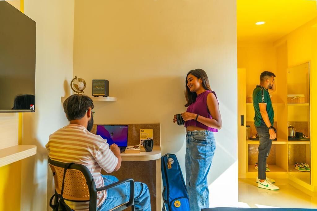 A hotel room with a desk, a laptop, a globe, and a shelf with items.