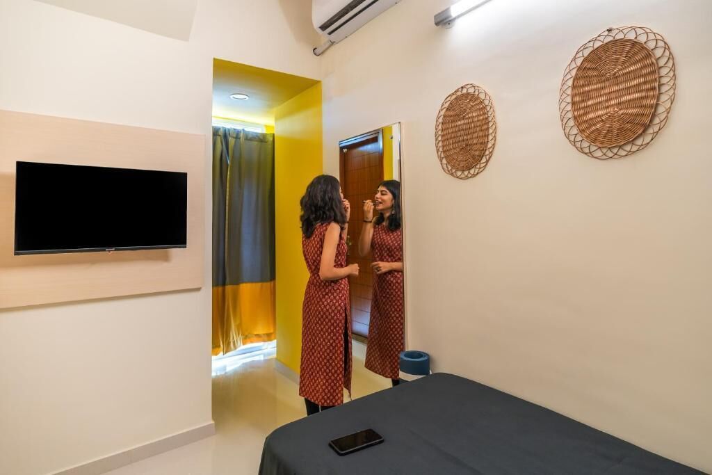 A hotel room with a bed, a flat-screen TV mounted on the wall, a mirror, and two woven wall decorations.