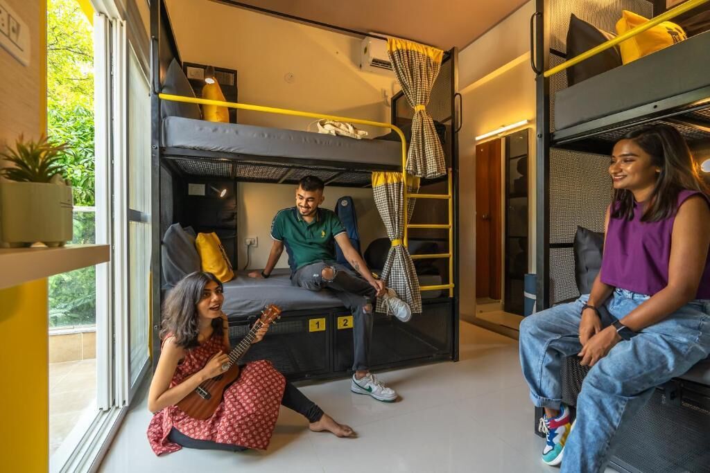 A compact, modern room with bunk beds, a small seating area, and a window providing a view of greenery outside.