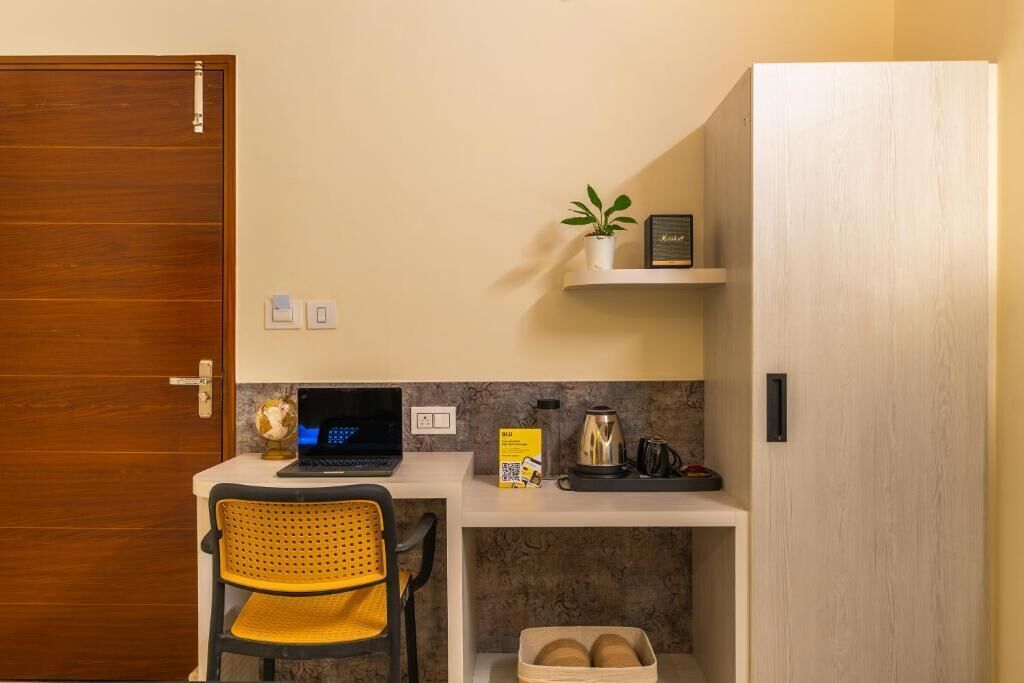 A compact kitchenette with a laptop, a small shelf with a plant, and a coffee maker.