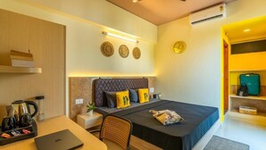 A modern hotel room with a bed, a desk with a laptop, a coffee maker, and a small plant.