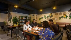 A group of people seated around a table in a restaurant with a modern interior, including a bookshelf and decorative wall elements.