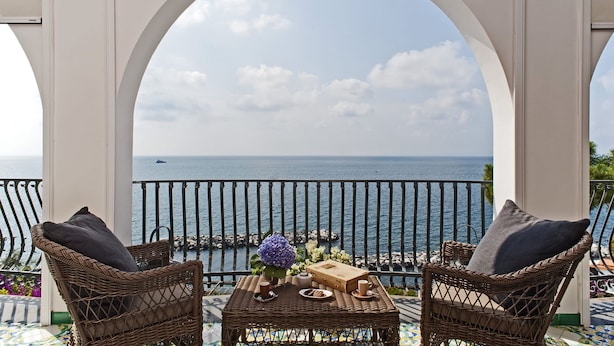 A balcony with wicker chairs, a table with a vase of flowers, and a view of the sea. - Villa Heart with private pool - My Rental Homes (Massa Lubrense)