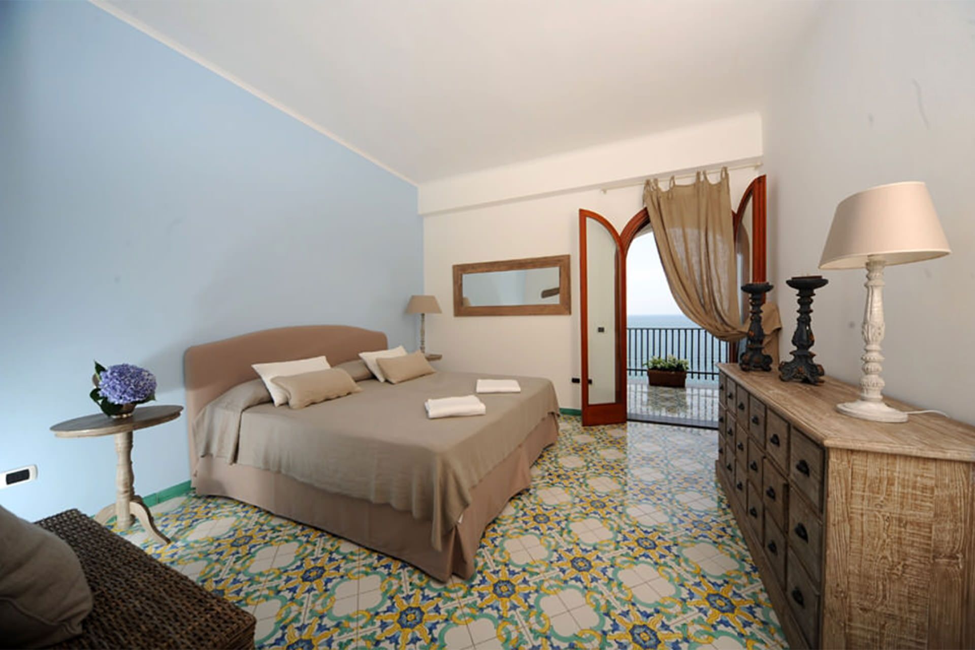 A bedroom with a bed, bedside table, lamp, dresser, and a view of the balcony.