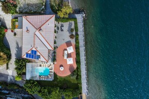 An aerial view of a coastal property with a swimming pool, a tennis court, and a circular patio area. - Villa Meridiana with lake view - My Rental Homes (Calozzo)