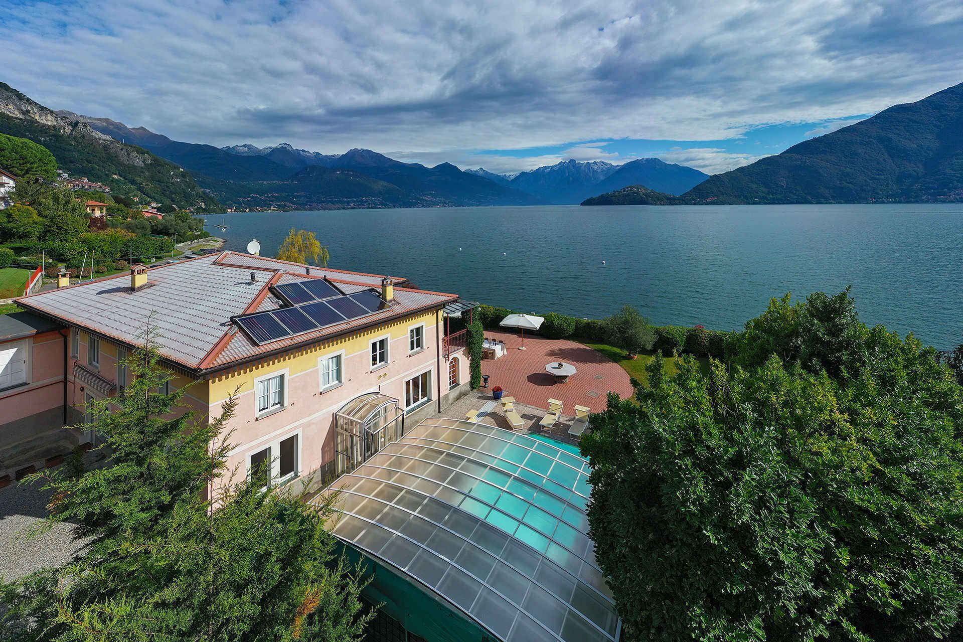 A house with a swimming pool, solar panels, and a view of a lake and mountains.