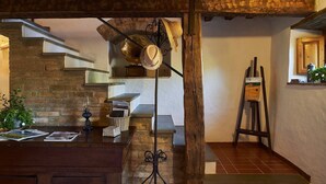 A rustic interior with exposed wooden beams, a staircase, a desk with magazines, and a painting on easels.