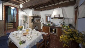 A rustic kitchen with exposed wooden beams, a fireplace, and a dining area set for a meal.