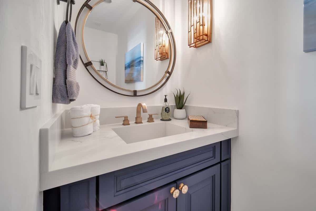 Une salle de bain moderne avec un meuble-lavabo blanc, un miroir rond, un porte-serviettes et une petite plante en pot.