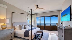 A modern hotel room with a large bed, a ceiling fan, a view of the ocean, and a television on the wall.