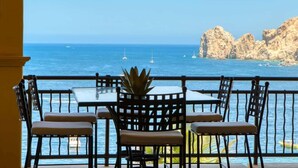 A balcony with a table and chairs overlooking the sea, with rocky cliffs in the background.