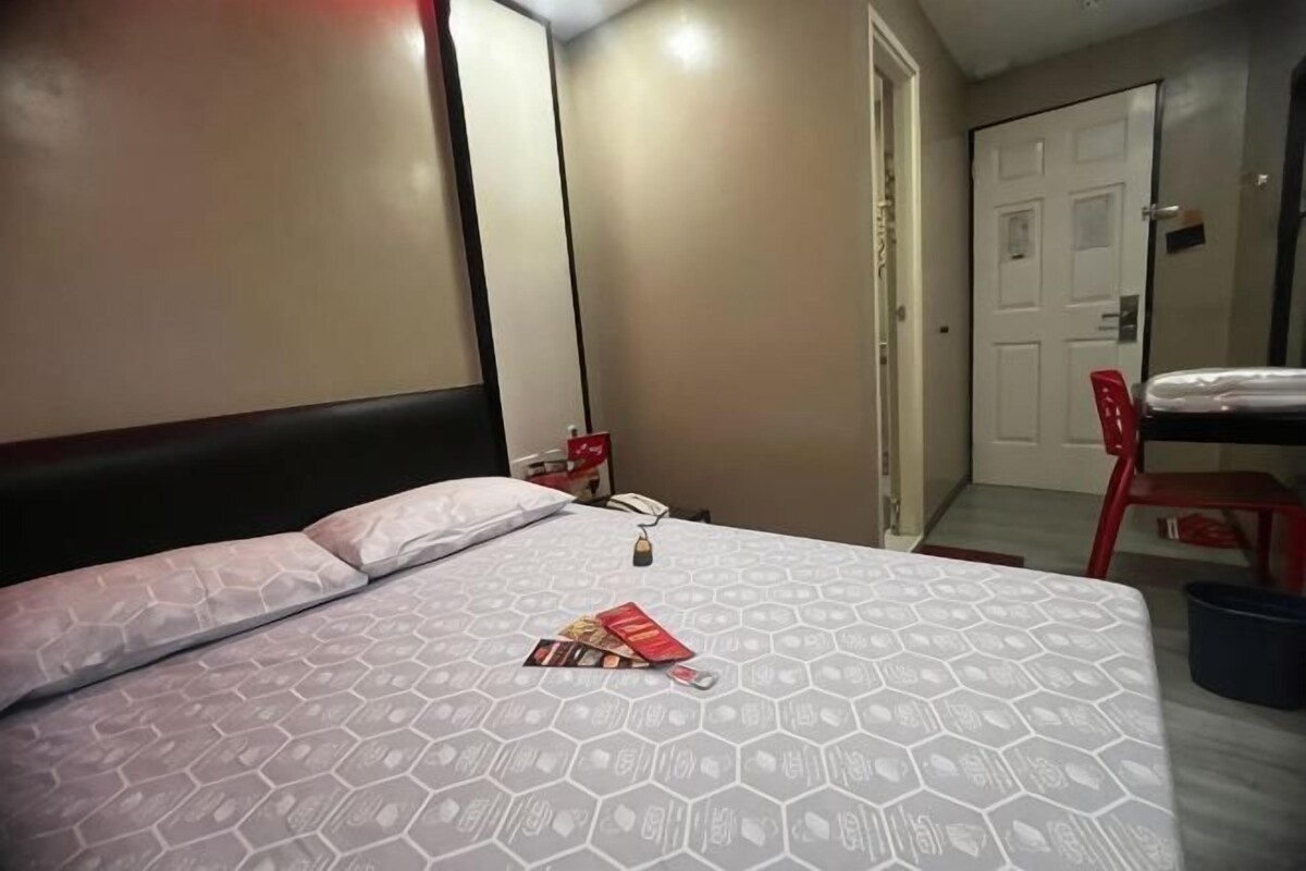 Una camera d'albergo con un letto, una sedia rossa, una porta e un tavolino con una bottiglia.