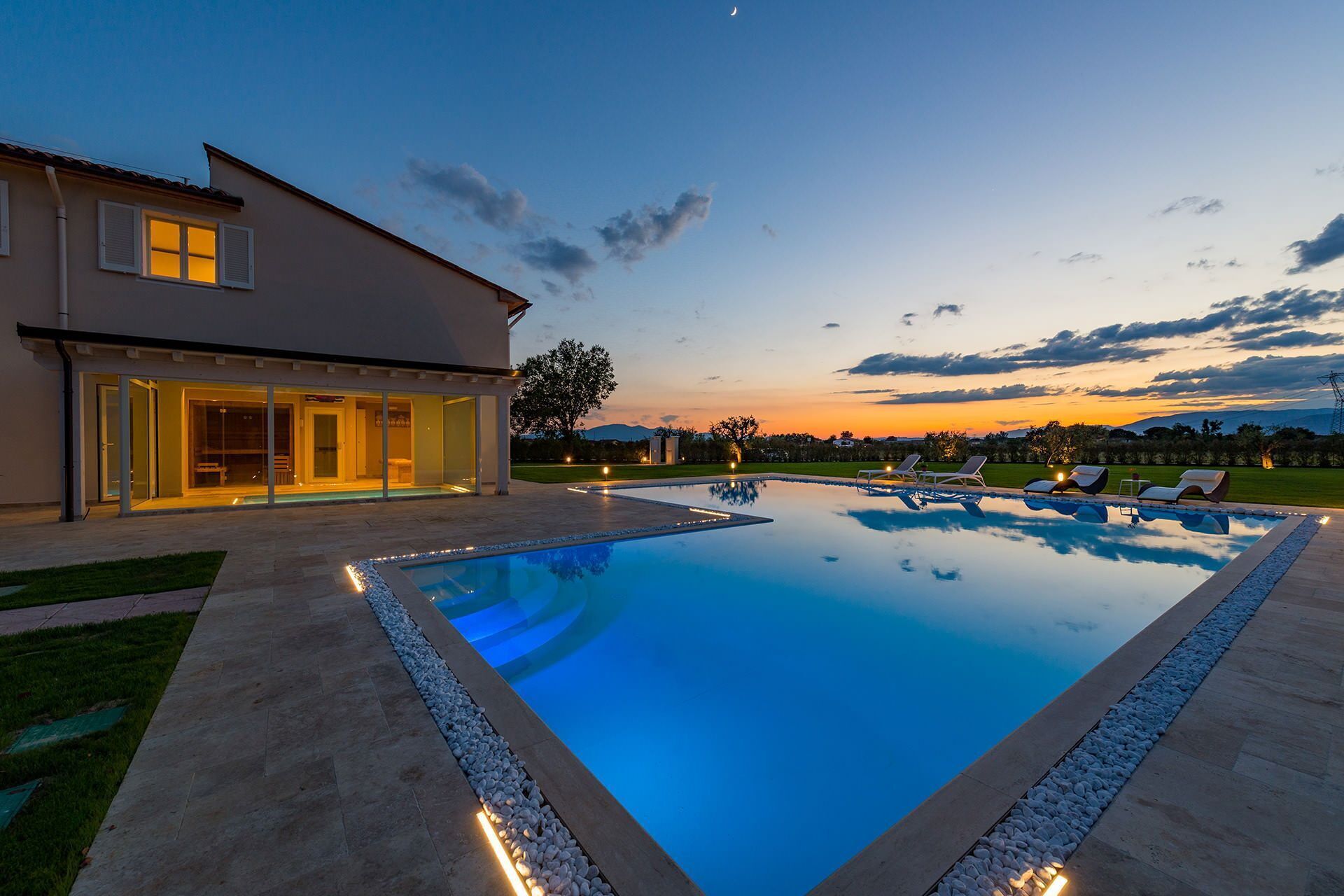 Ett modernt hus med en swimmingpool och solstolar.