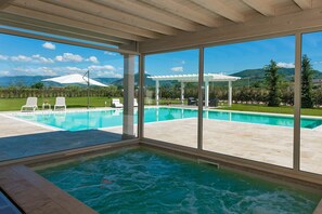 En modern inomhuspool med en vacker utsikt över en frodig trädgård och berg.