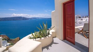 Un bâtiment aux murs blancs et à la porte rouge, qui offre une vue dégagée sur une mer bleue et des montagnes lointaines.