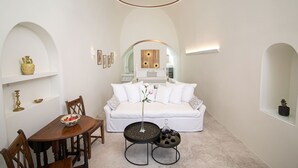 Une pièce blanche comprenant un lit, une table à manger avec des chaises et une petite table sur laquelle se trouvent un vase et un bol.
