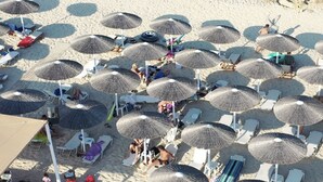 Luchtbeeld van een strand met tal van rieten parasols en ligbedden in rijen.
