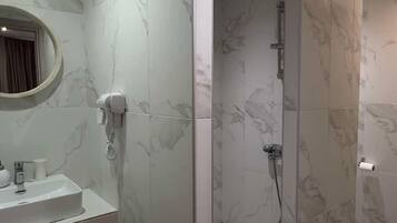 Un baño moderno con cabina de ducha revestida de mármol, un lavabo con espejo y un inodoro.