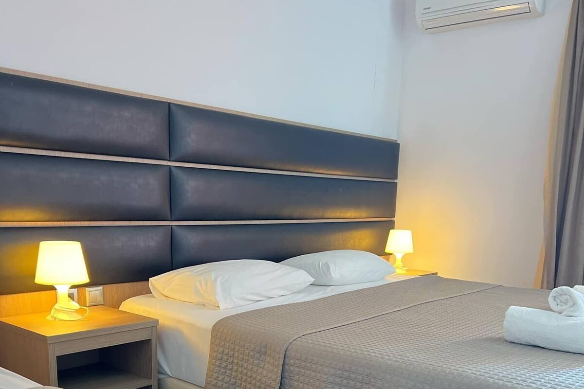 Ein Hotelzimmer mit zwei Betten, einem Kopfteil, Nachttischlampen, einem gefalteten Handtuch und einer Klimaanlage.