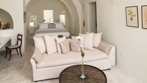 A spacious living room with a white sofa, a round coffee table, and a large circular ceiling light fixture. - My Rental Homes - Aloy Suite with outdoor hot tub, covered Jacuzzi and sea view (Fira)