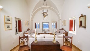 A dining area with a wooden table and chairs, a chandelier, and a view of the sea through a window. - My Rental Homes - Palea Suite with Jacuzzi, sea view e wonderful rooftop terrace (Fira)