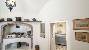 A hallway with a rustic stone fireplace, shelves with pottery, and framed pictures on the walls. - My Rental Homes - Palea Suite with Jacuzzi, sea view e wonderful rooftop terrace (Fira)