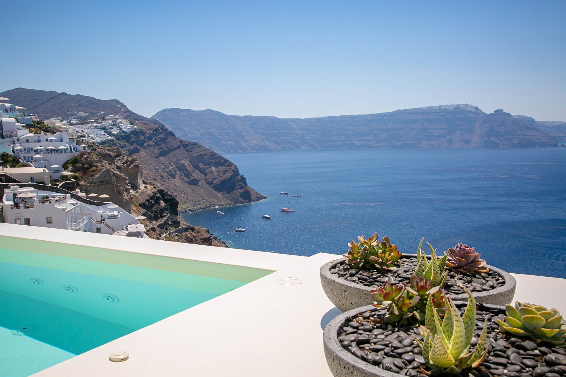 A pool with a clear view of a coastal landscape, including white buildings and a mountainous backdrop.